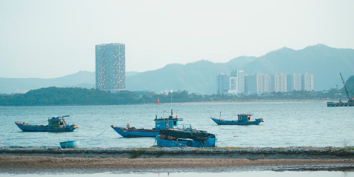 Scenic view of fishing boats in Da Nang harbor with urban skyline and mountains.